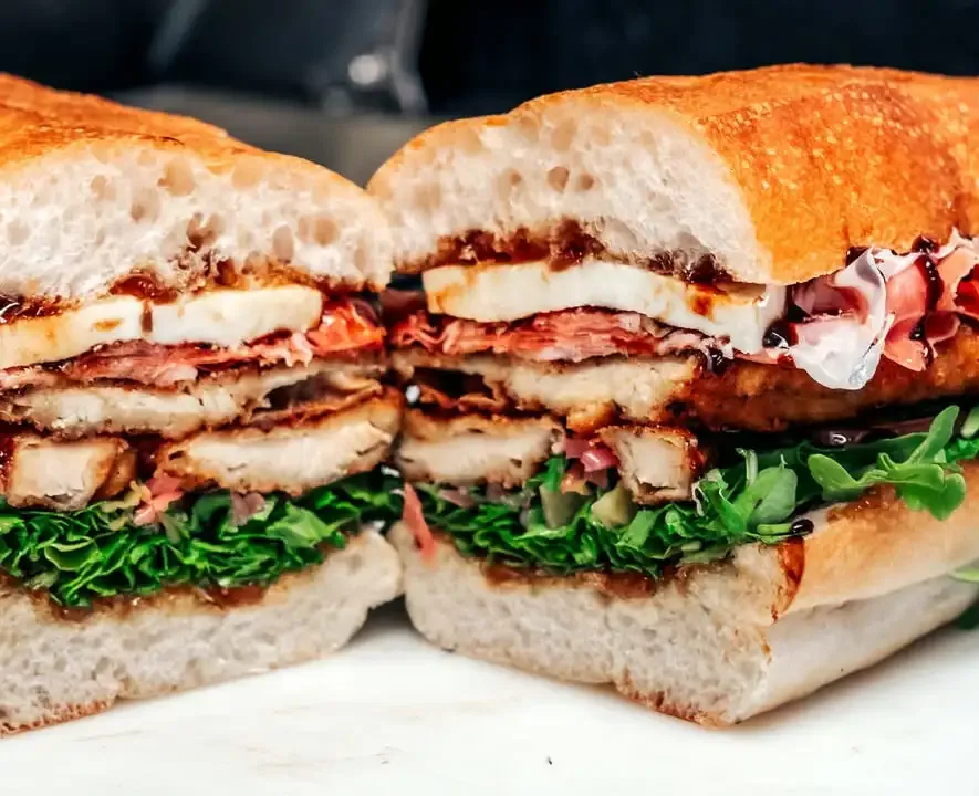 A grinder cut in half, stacked with chicken cutlet, prosciutto, fresh mozzarella and arugula