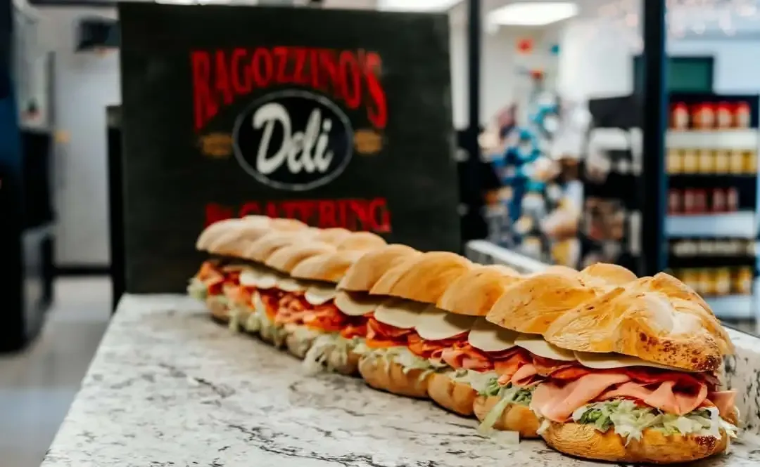 A party-length grinder on the counter in front of the Ragozzino's Deli & Catering sign