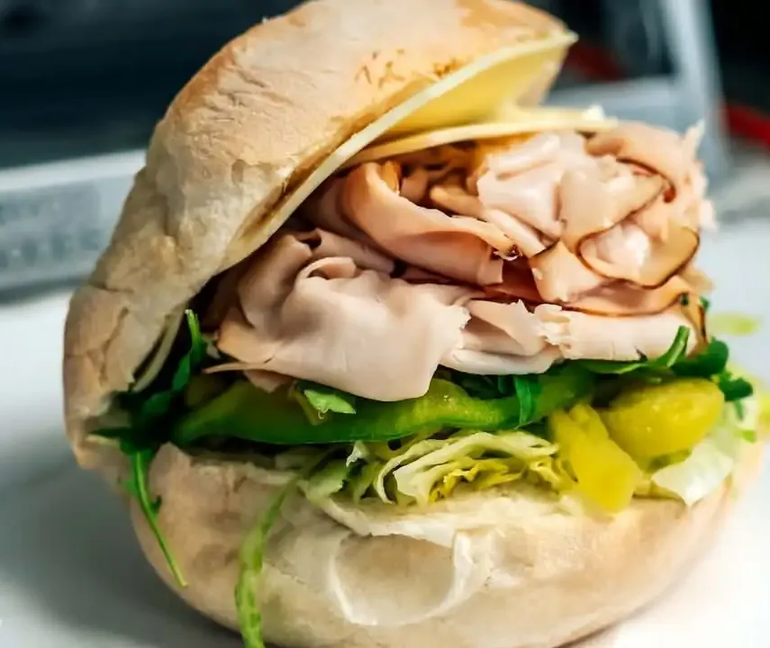 A turkey grinder on a hard roll with lettuce, green peppers and banana peppers